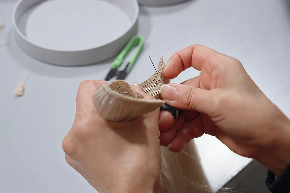Close-up of an Epoche worker hand sewing and securing a clip to a human hair clip-in extension