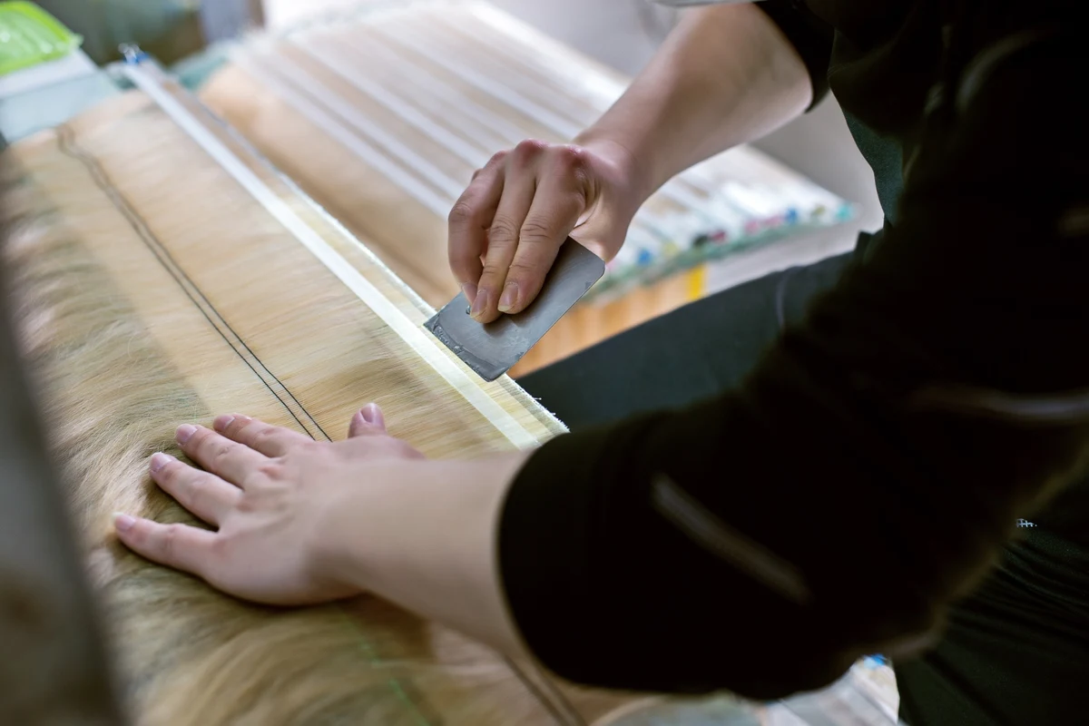 Epoche worker removing air bubbles from tape-in hair extension adhesive during production