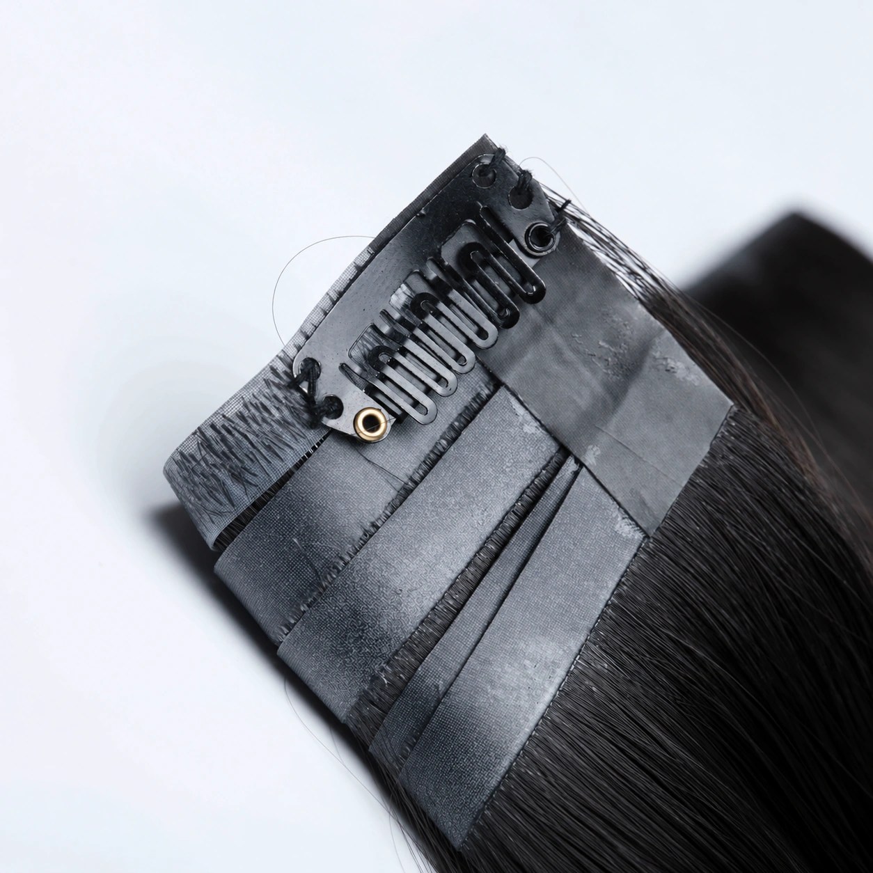Close-up of a black snap clip and stitching on the gray base of dark clip-in hair extensions.