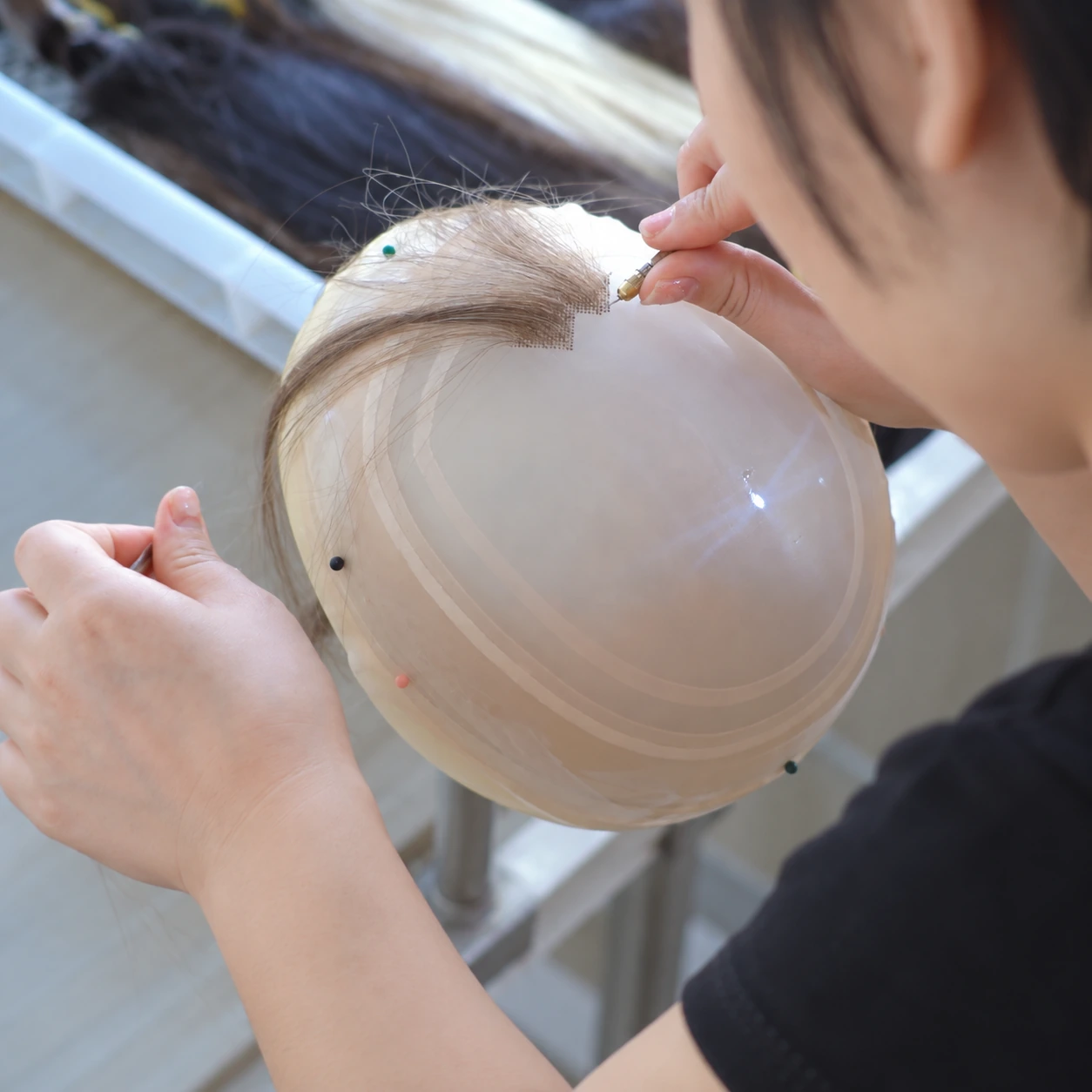 Hair Topper Hand Ventilation Process | Epoche Hair Worker in a black short-sleeve shirt hand-knotting light blonde hair into lace on a rounded support.