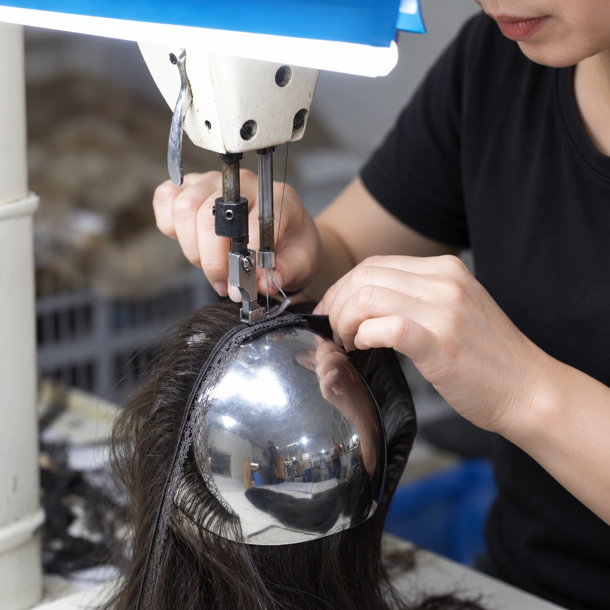 Hair Extension Band Sewing Process | Epoche Hair Worker guiding a dark hair extension band under an industrial sewing machine needle over a rounded metal support.