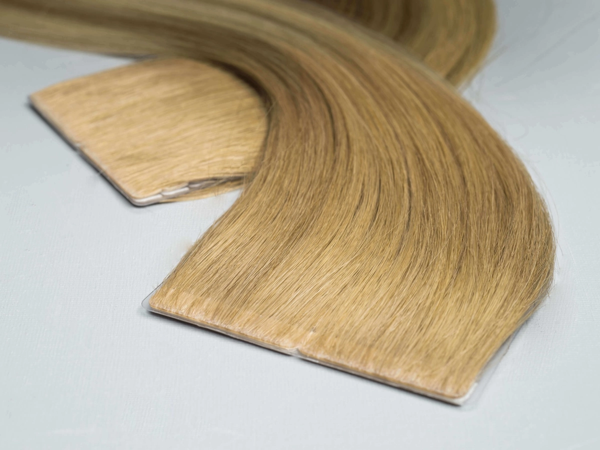 Invisible Tape-In hair extensions arranged in overlapping curves on a pale surface, with hair covering the tape tabs.